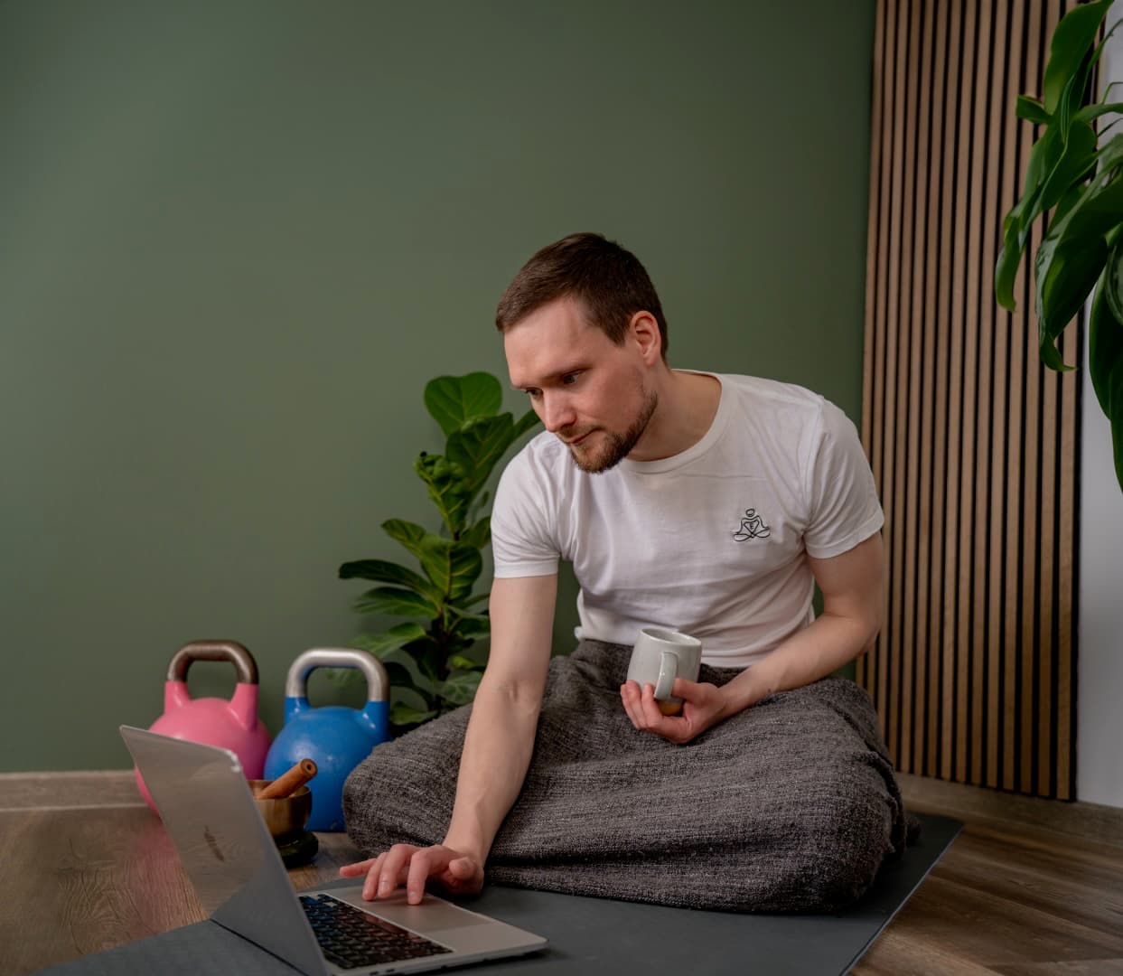 Entspannungstrainer Johannes bei Online-Coaching Session mit Laptop und Kaffee, umgeben von Trainingsgeräten und Zimmerpflanzen in entspannender Atmosphäre