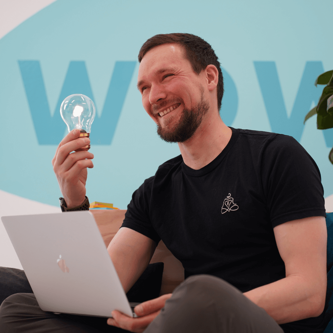 Innovative Entspannungsmethoden - Online Kurse von Entspannungshelden Johannes hält lächelnd Glühbirne - Entspannungshelden Gründer bei der Ideenfindung am Laptop